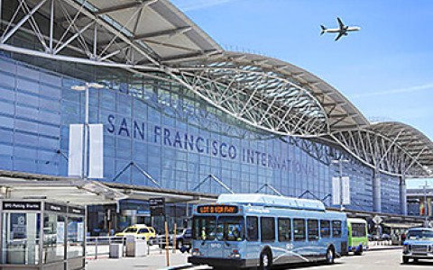 San Francisco International Airport with an airplane above it in the sky and blue busses outfront